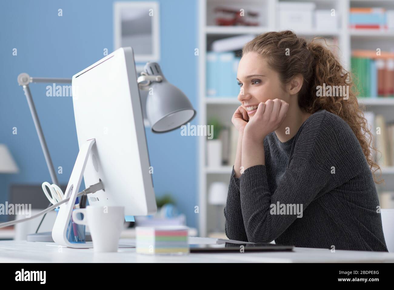 Junge lächelnde schöne Frau mit einem Computer im Büro und einer Online-Verbindung sieht sie Videos und Filme Stockfoto