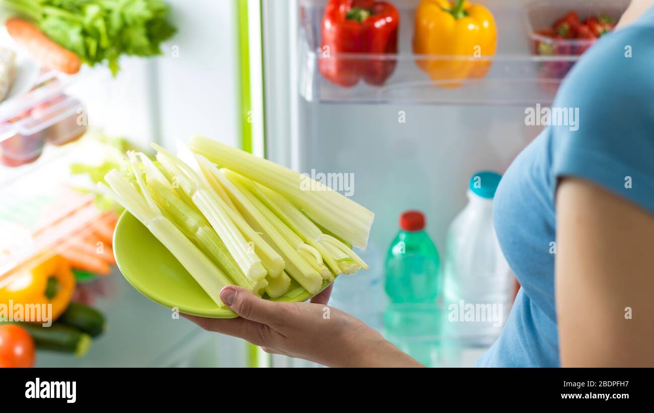 Frau, die frischen Sellerie aus dem Kühlschrank mitnimmt und zu Hause eine gesunde Mahlzeit zubereitet Stockfoto