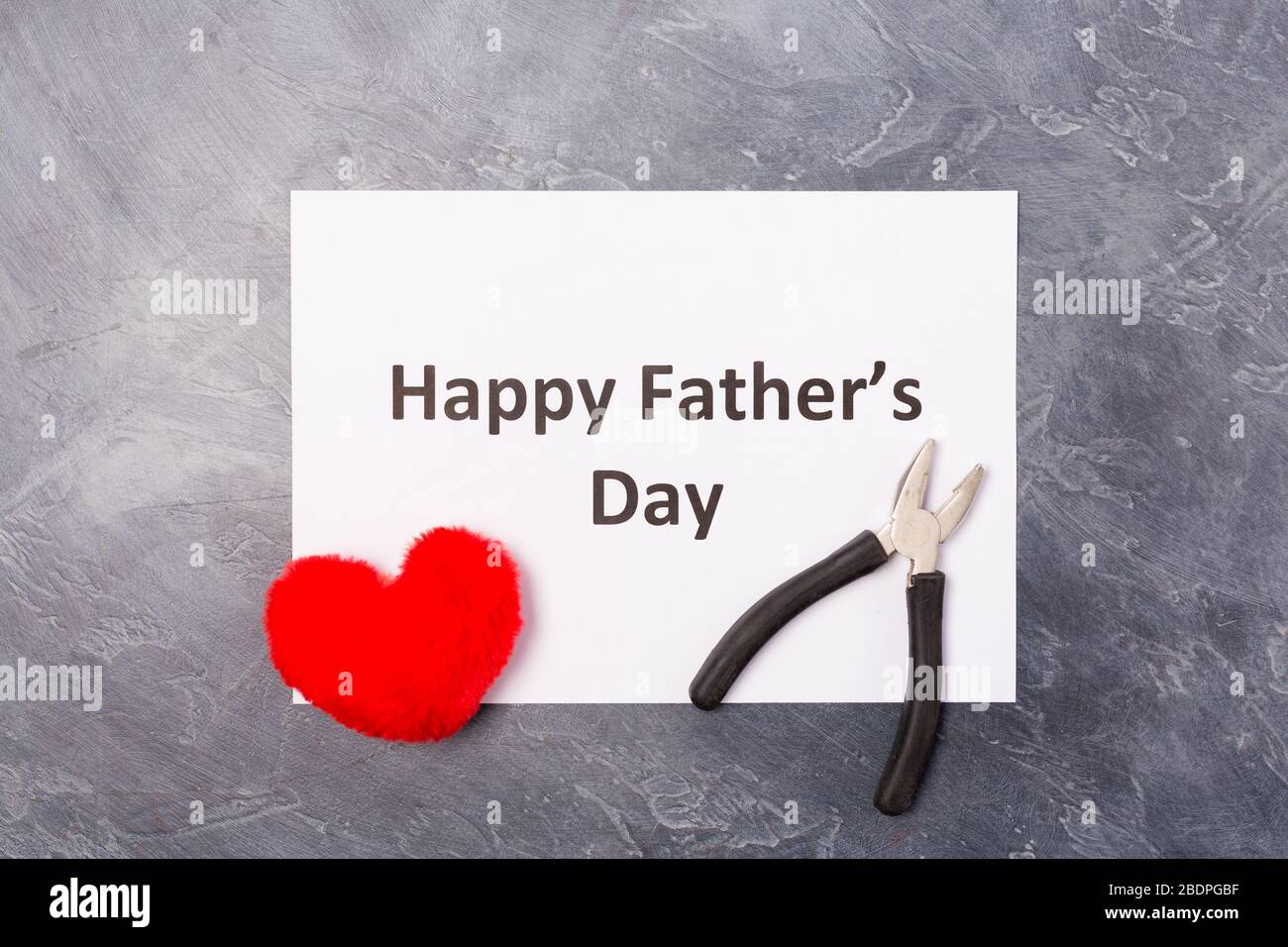 Happy Father's Day Text auf handwerkseigenen Umschlag auf grauem Hintergrund mit rotem Herz und Zange. Freier Speicherplatz. Leerzeichen für Text. Vatertag Urlaubskonzept. Stockfoto