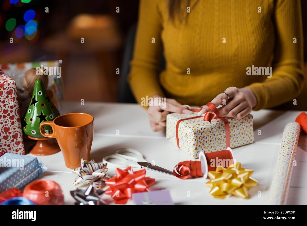 Frau, die zu Hause Weihnachtsgeschenke einwickelt, bindet sie einen Bandbogen: Feiertags- und Festtagskonzept Stockfoto