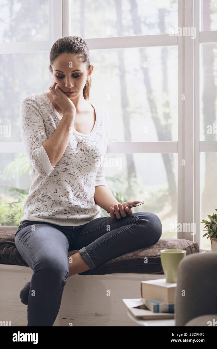 Traurige Frau, die auf ihrem Telefon schlechte Nachrichten erhält, ist sie herzzerreißend und blickt nach unten Stockfoto