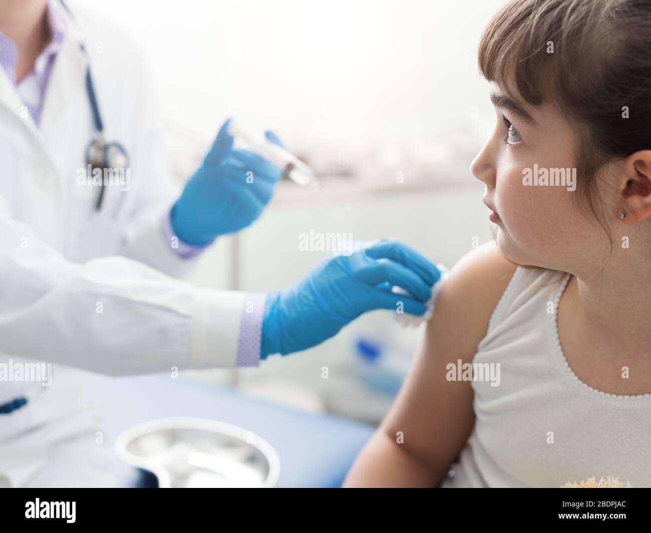 Doktor, der einem erschrockenen jungen Kind eine Injektion verabreicht, das Mädchen ist verängstigt und schaut auf die Spritze Stockfoto