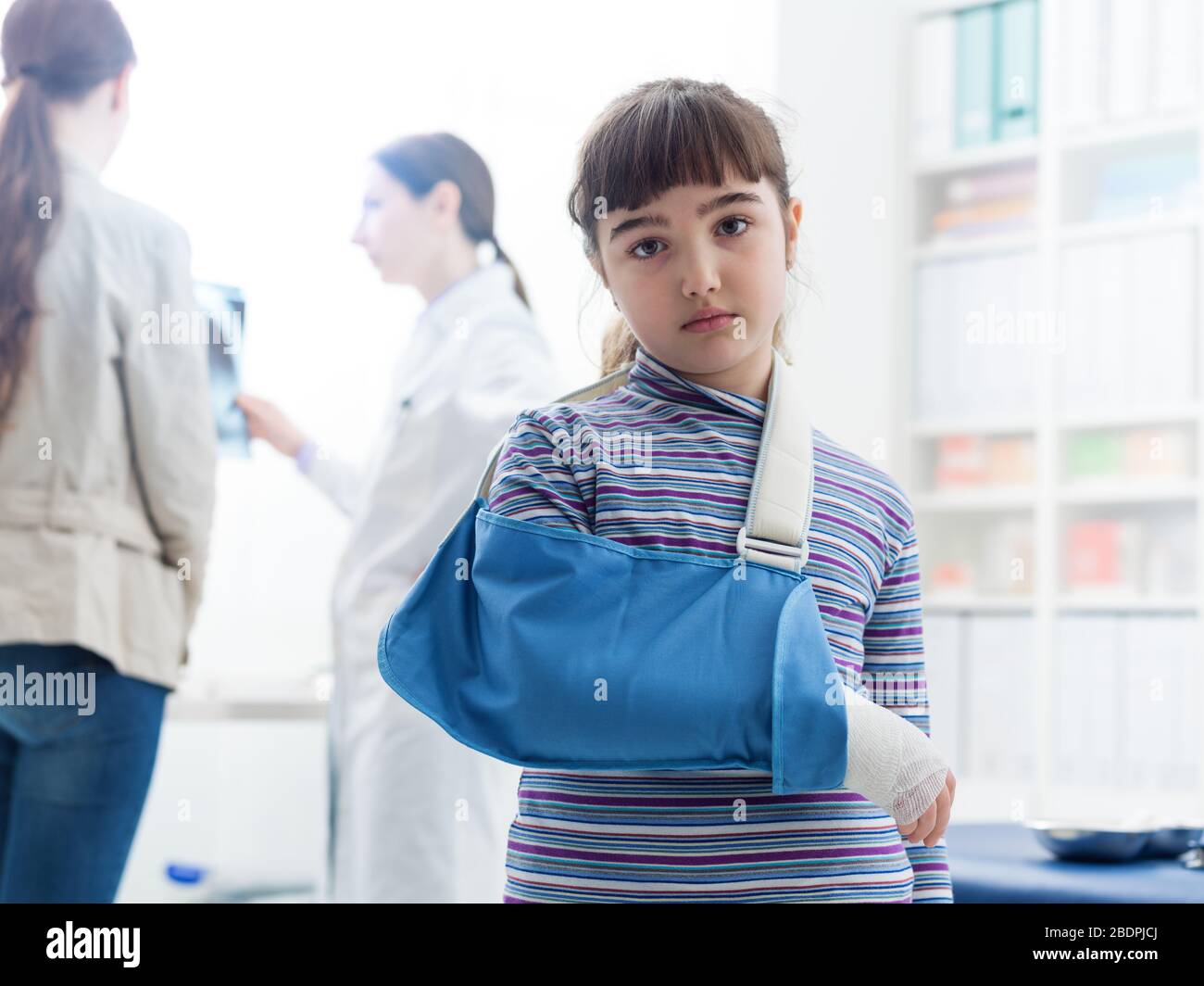 Süßes trauriges Mädchen mit gebrochenem Arm in der Arztpraxis trägt sie eine Armstütze und blickt auf die Kamera Stockfoto