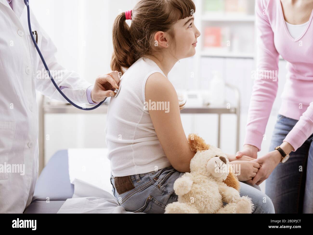 Weibliche Ärztin untersucht ein süßes lächelndes Mädchen mit einem Stethoskop, die Mutter ist neben ihr, Kinder- und Gesundheitskonzept Stockfoto