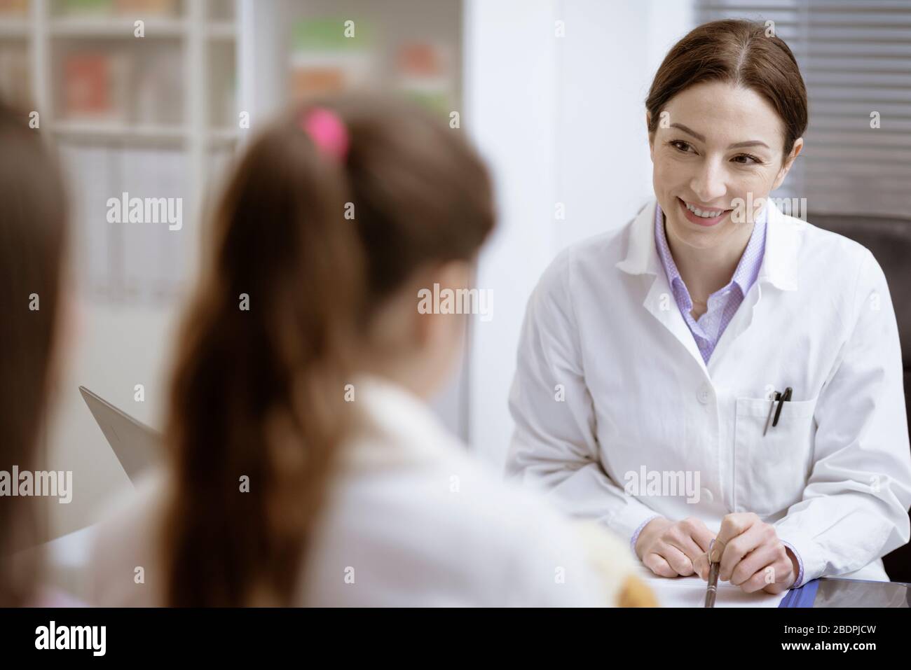 Weibliche Ärztin sitzt am Schreibtisch und begeht Patienten im Büro, sie lächelt und überprüft die Krankenakten Stockfoto