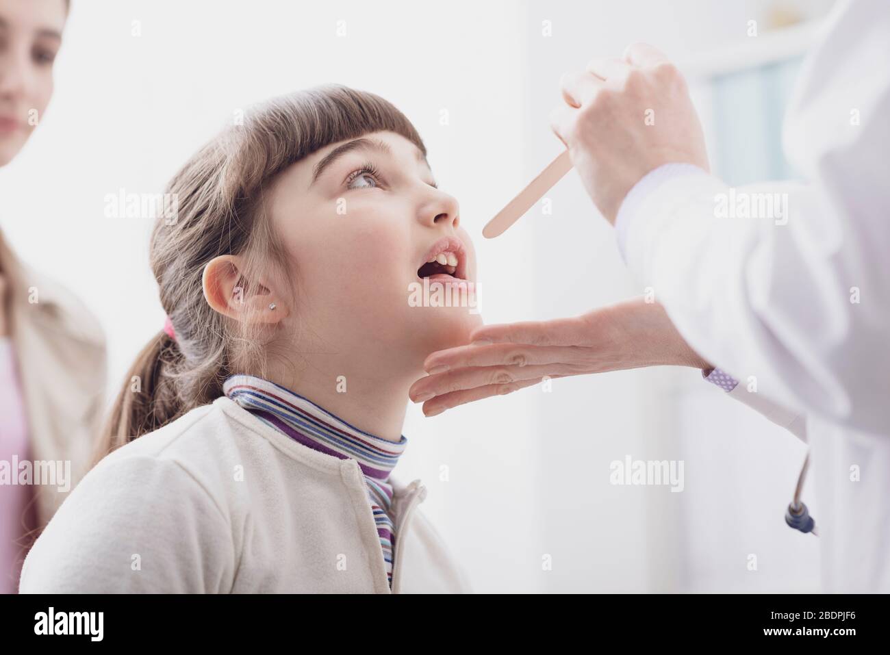 Professionelle Ärztin überprüft die Kehle eines Mädchens, sie öffnet ihren Mund Stockfoto