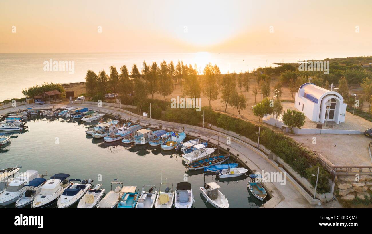 Luftbild des Sonnenuntergangs an der Küste und die weiße, gewaschene Kapelle am Strand Agia Triada, Protaras, Famagusta, Zypern von oben. Vogelperspektive auf Tour Stockfoto