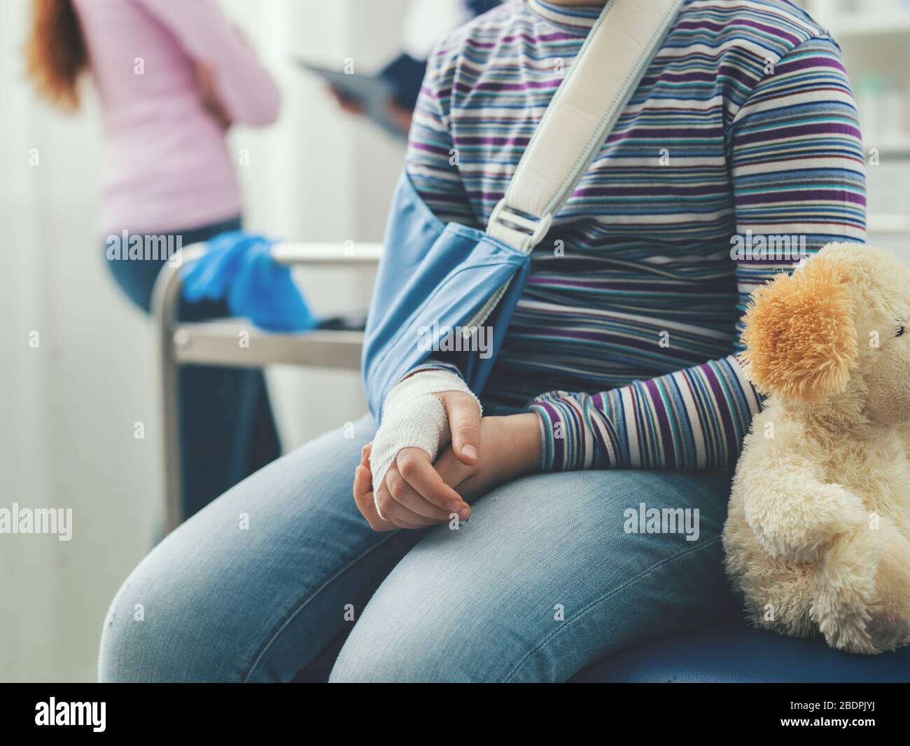 Süßes Mädchen in der Arztpraxis, das auf einen Besuch wartet, sitzt sie mit ihrem Teddybären auf der Untersuchungskecke Stockfoto