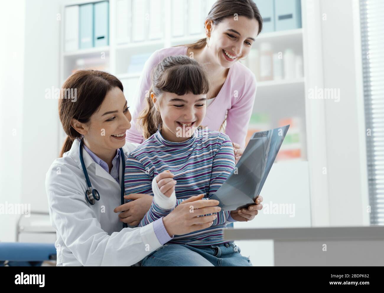 Freundlicher Arzt, der ein Mädchen auf dem Schoß hält und ihr ein Röntgenbild ihres Arms zeigt Stockfoto