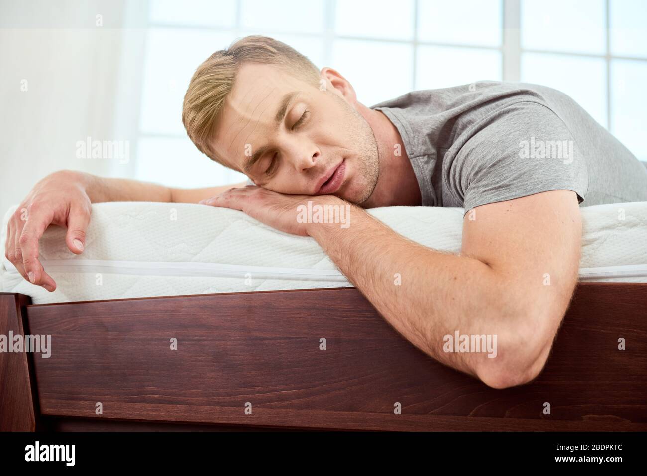Junger schöner Mann schläft auf einer großen und komfortablen orthopädischen weißen Matratze im Schlafzimmer. Ein Nickerchen machen. Müde fühlen. Startseite Stockfoto