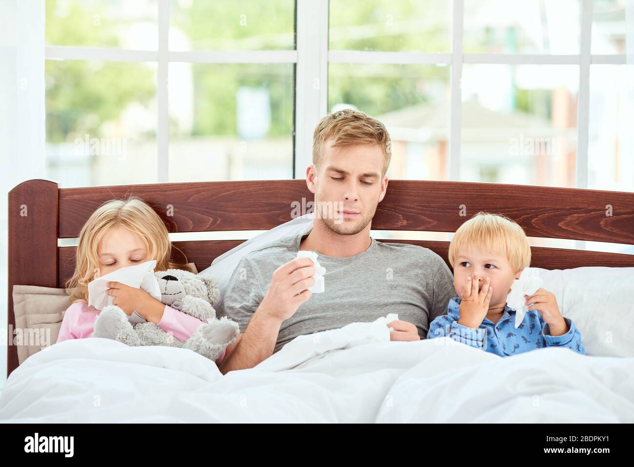 Kranke Familie von drei mit laufender Nase, die zu Hause zusammen im Bett liegt. Viruserkrankung. Coronavirus-Konzept. Kranke Familie zu Hause. Gesundheitskonzept Stockfoto