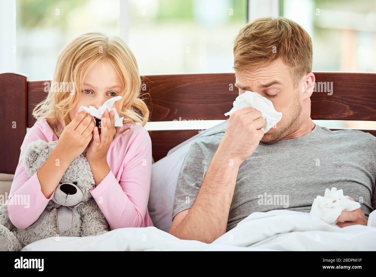 Der junge Vater und seine Tochter leiden an Grippe oder kalter und laufender Nase, während sie zu Hause zusammen im Bett liegen. Viruserkrankung. Coronavirus-Konzept. Kranke Familie zu Hause. Gesundheitskonzept Stockfoto