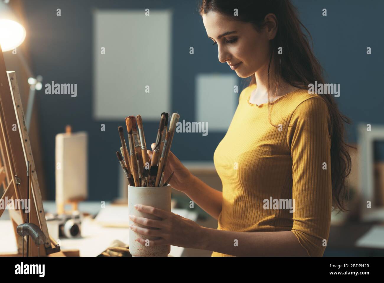 Junge Frau malt im Atelier und wählt die richtige Bürste für ihr Kunstwerk Stockfoto