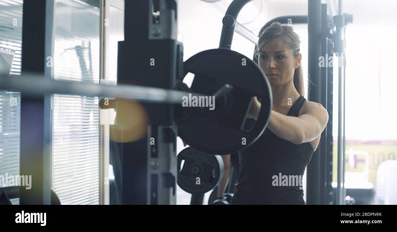Athletische Passform Frau Gewichtheben im Fitnessstudio und Krafttraining: Sie bereitet eine Barglocke für das Workout vor Stockfoto