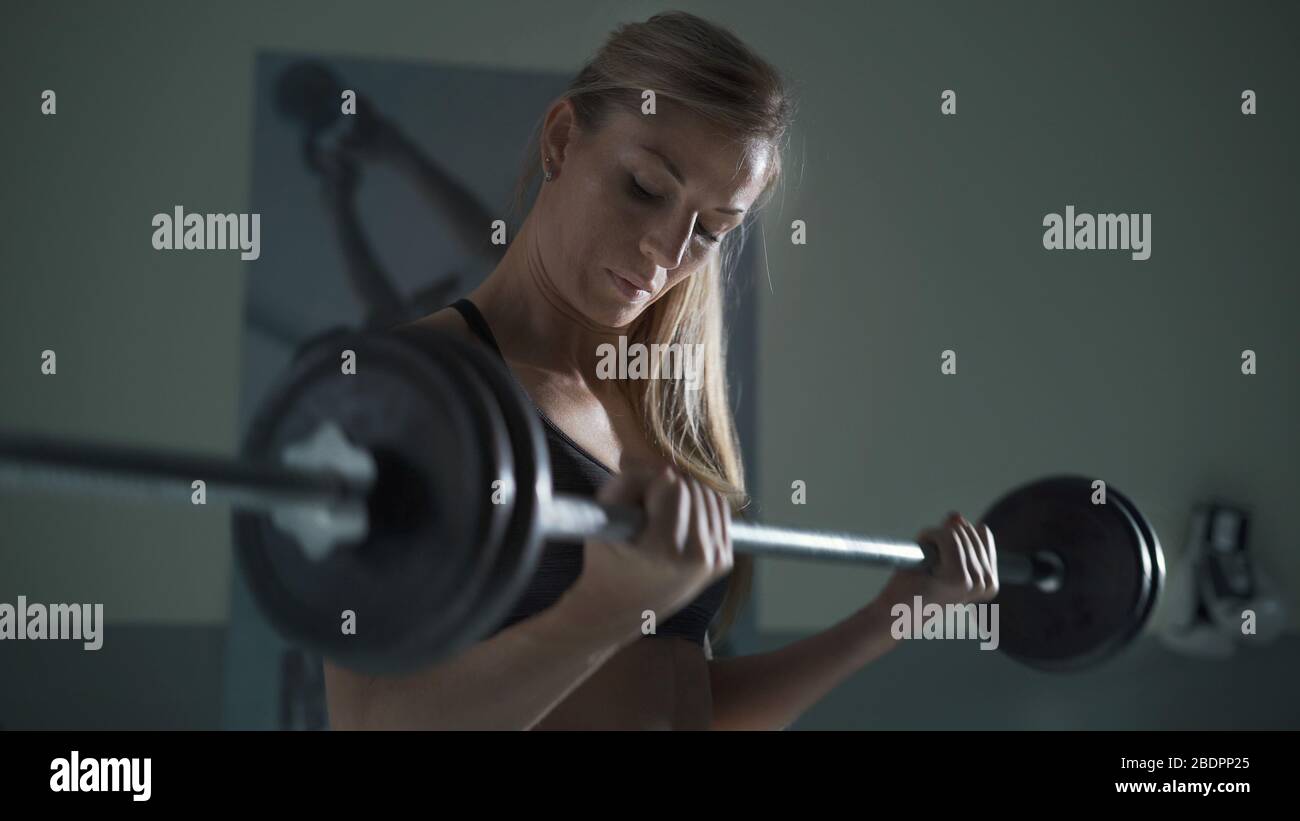 Athletische Bodybuilderin, die in der Turnhalle arbeitet, macht sie mit einer Barglocke Gewichtheben Stockfoto