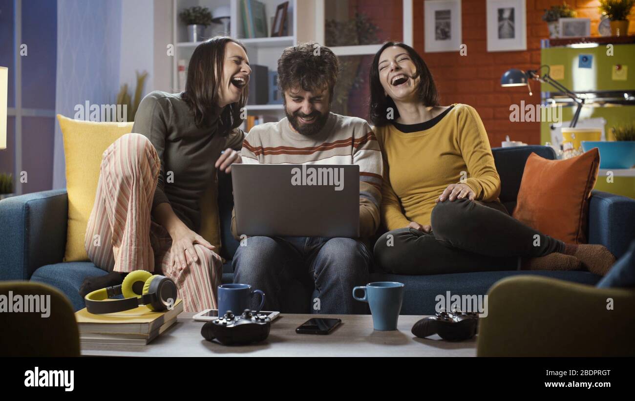 Fröhliche Freunde sitzen zu Hause auf dem Sofa und verbinden sich online mit ihrem Laptop, sie sind soziale Netzwerke und haben Spaß Stockfoto