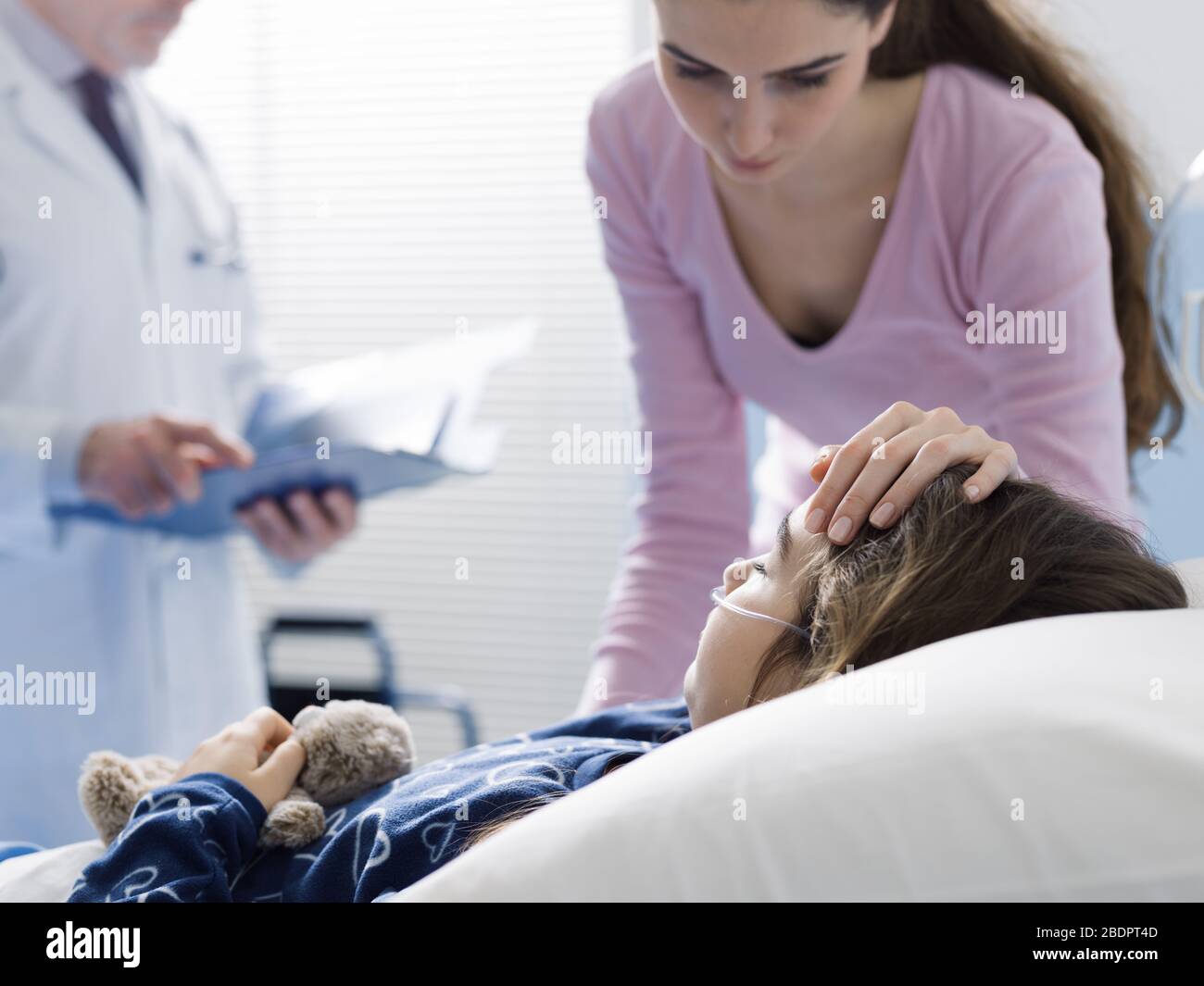 Ein Kind, das im Bett im Krankenhaus liegt, ein Arzt und ihre Mutter sind neben ihr, der Pädiatrie und dem Gesundheitskonzept Stockfoto