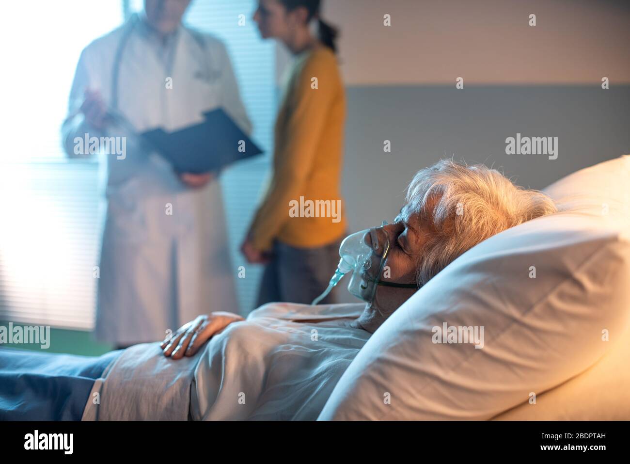 Leitender Patient im Bett liegenden Krankenhaus und Arzt im Hintergrund mit einem Familienmitglied sprechen Stockfoto
