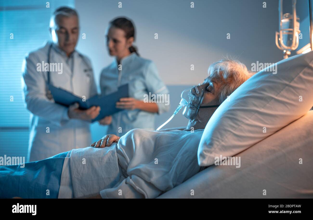 Leitender Patient im Bett liegen und medizinisches Personal spricht im Hintergrund, Oberpflegekonzept Stockfoto