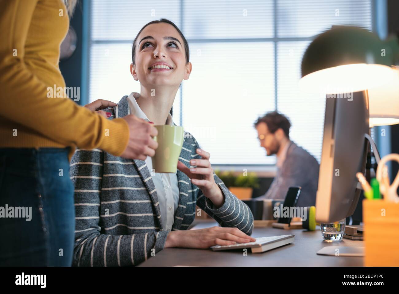 Kollegen, die im Büro zusammenarbeiten und eine Kaffeepause einlegen, nimmt die Frau eine Tasse und lächelt Stockfoto