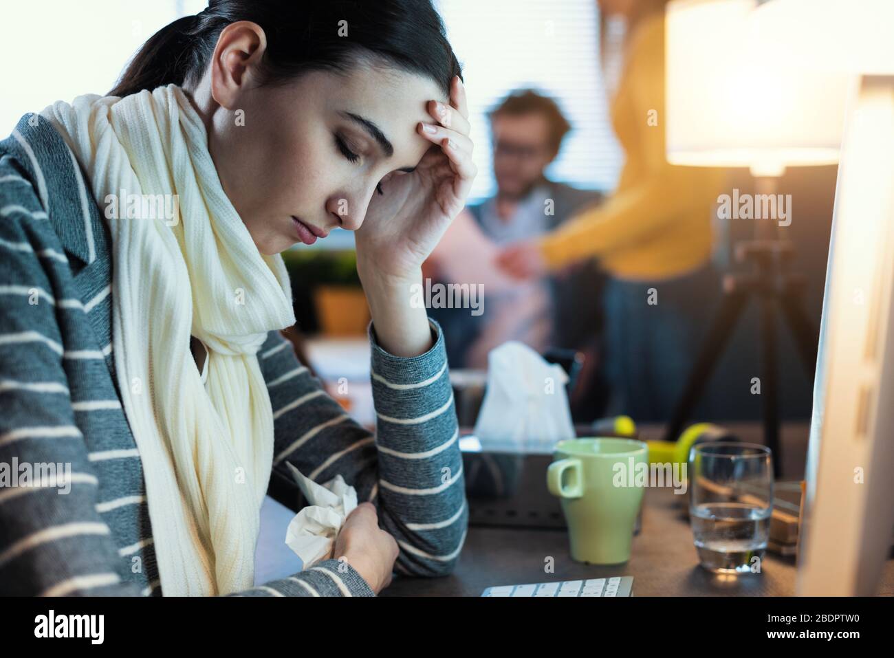 Junge Frau, die am Schreibtisch arbeitet und sich unwohl fühlt, hat Fieber und Kopfschmerzen Stockfoto