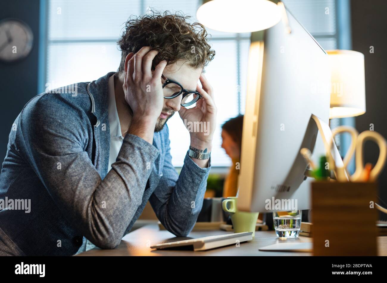 Gestresster Büroangestellter sitzt am Schreibtisch und arbeitet mit seinem Computer, er ist müde und hat Kopfschmerzen Stockfoto