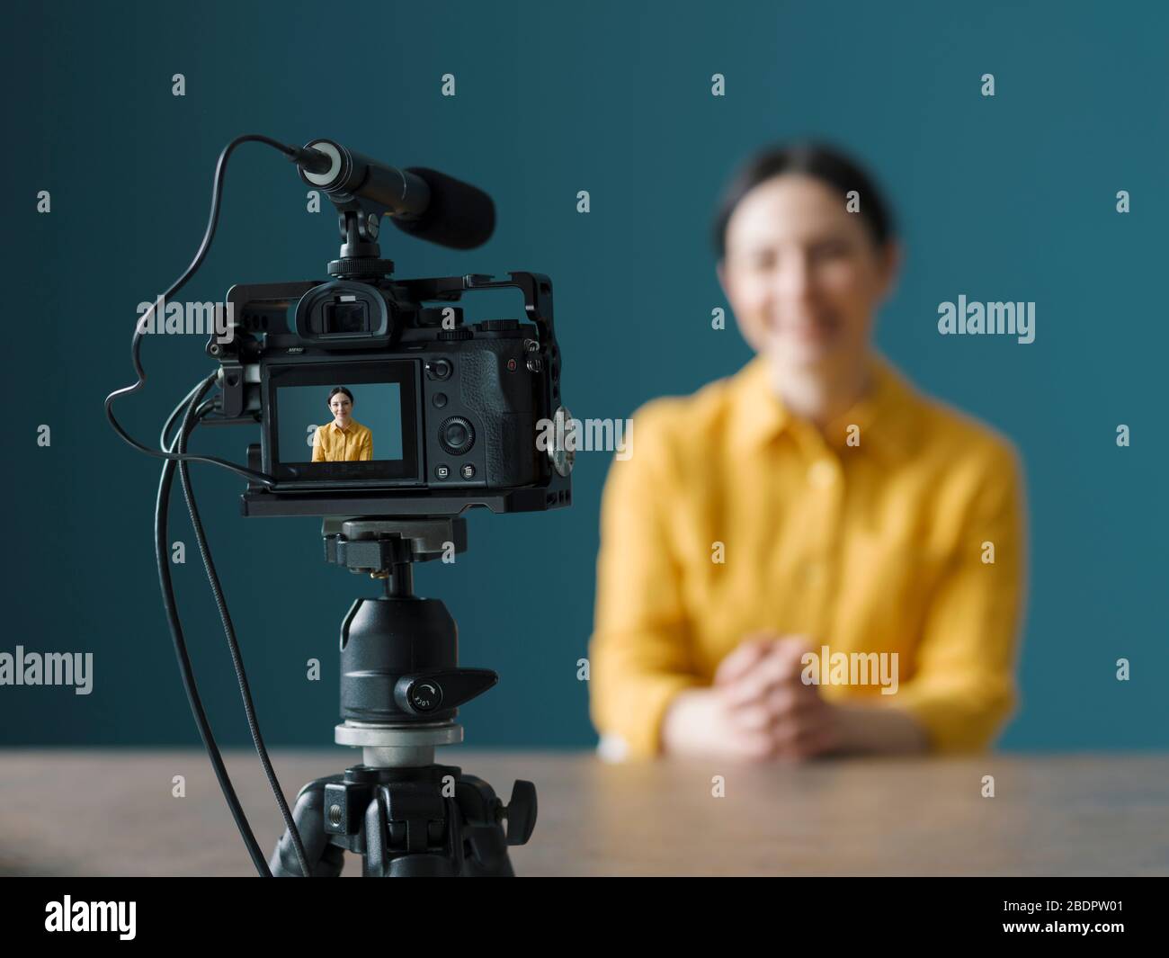 Lächelnde Frau, die vor einer Kamera sitzt und einen Videoblog macht Stockfoto