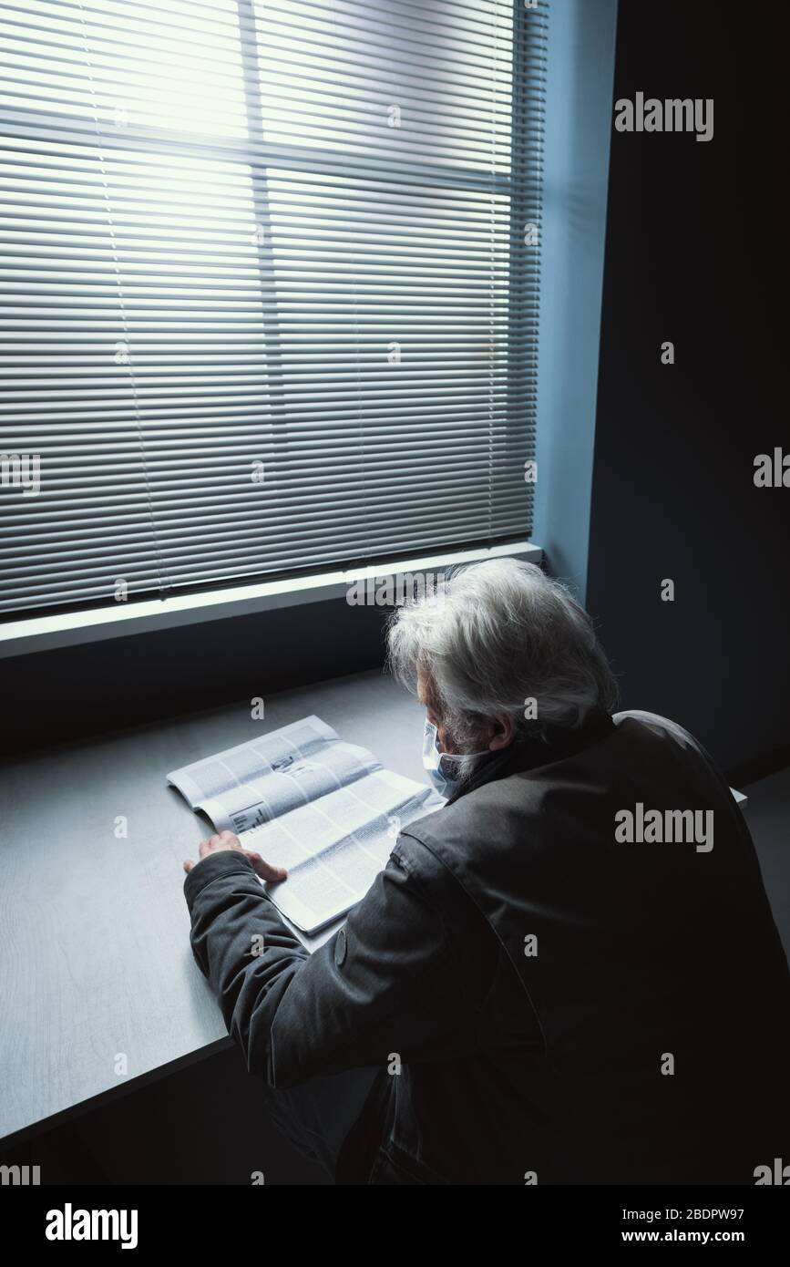 Einsame Senioren sitzen allein zu Hause, tragen eine Gesichtsmaske und lesen eine Zeitung, Virus-Notfallmaßnahmen und ein älteres Sicherheitskonzept Stockfoto