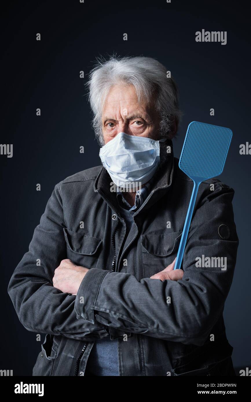 Selbstbewusster Senior schützt sich vor dem Virus Covid-19, er trägt eine chirurgische Maske und hält einen Schwatter Stockfoto