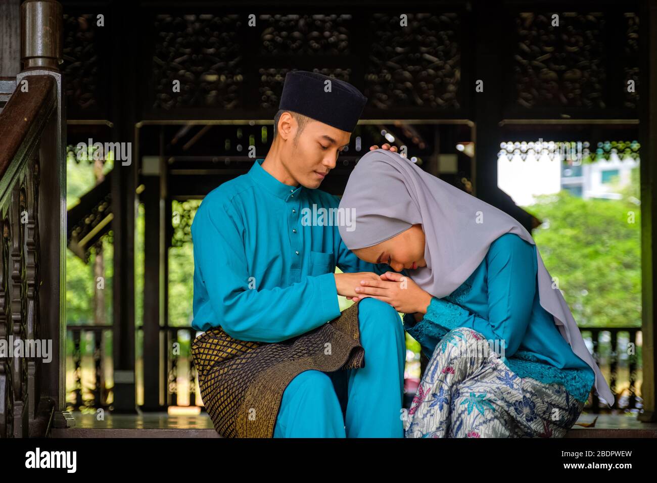 Junges Paar malaiischer moslem in traditioneller Tracht, das während der Aidilfitri-Feier im traditionellen Holzhaus eine entschuldigende Geste zeigt. Raya und Musl Stockfoto