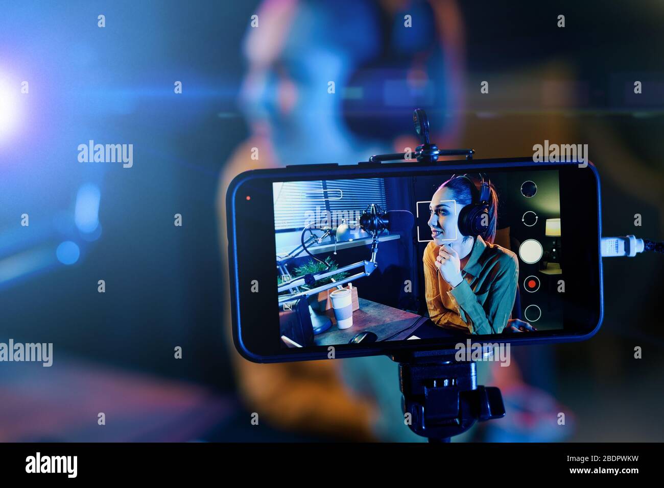 Junge Frau streamt mit ihrem Smartphone ein Live-Video und spricht mit einem Mikrofon im Studio Stockfoto