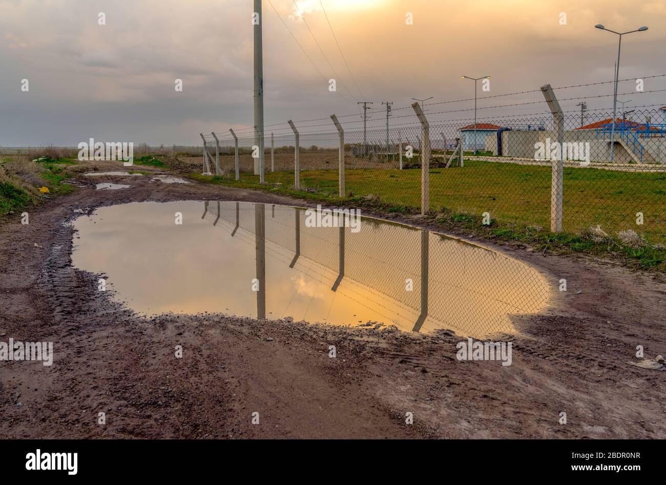 Pfütze auf Erdstraße in der Nähe von Drahtgefleinen bei Sonnenuntergang Stockfoto