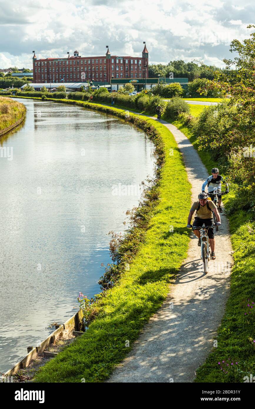 Radfahrer auf dem Weg von Leeds und Liverpool Canal in der Nähe von Chorley, Lancashire. Botany Bay Mühle dahinter. Stockfoto