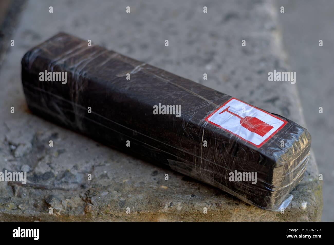 Das Lieferpaket liegt auf den Stufen. Auf Beton liegt eine schwarze Schachtel mit einem zerbrechlichen Schild. Leicht zu stehlen. Unvorsichtige Haltung gegenüber Paketen. Selektiver Fokus Stockfoto