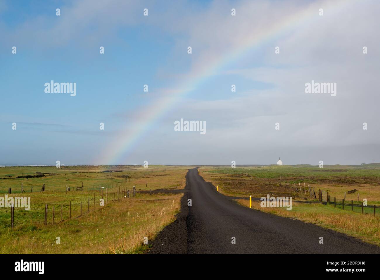 Ein Regenbogen über der asphaltierten Straße nach Strandarkirkja im Süden Islands Stockfoto