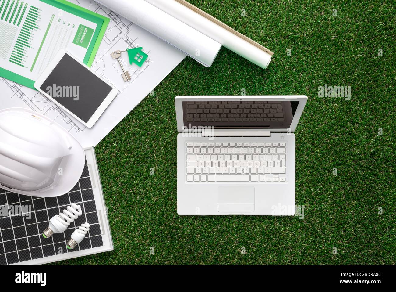 Hausprojekt, Solarpanel, Schutzhelm und Laptop auf üppigem Gras, grünes, nachhaltiges Gebäude und alternatives Energiekonzept Stockfoto