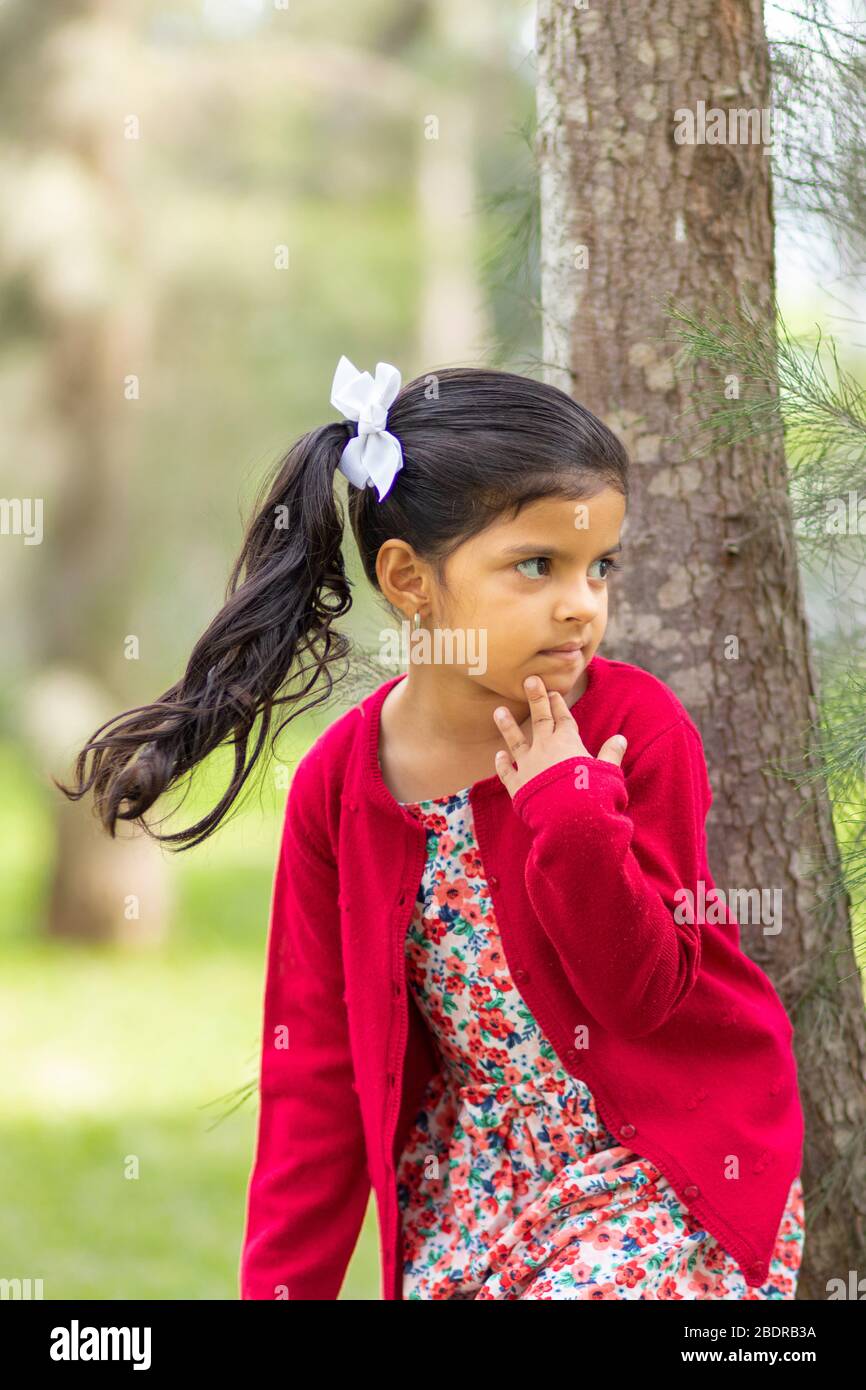 Kleines Mädchen in Blumenkleid und roten Pullover, sehr glücklich und lächelnd im Wald Stockfoto