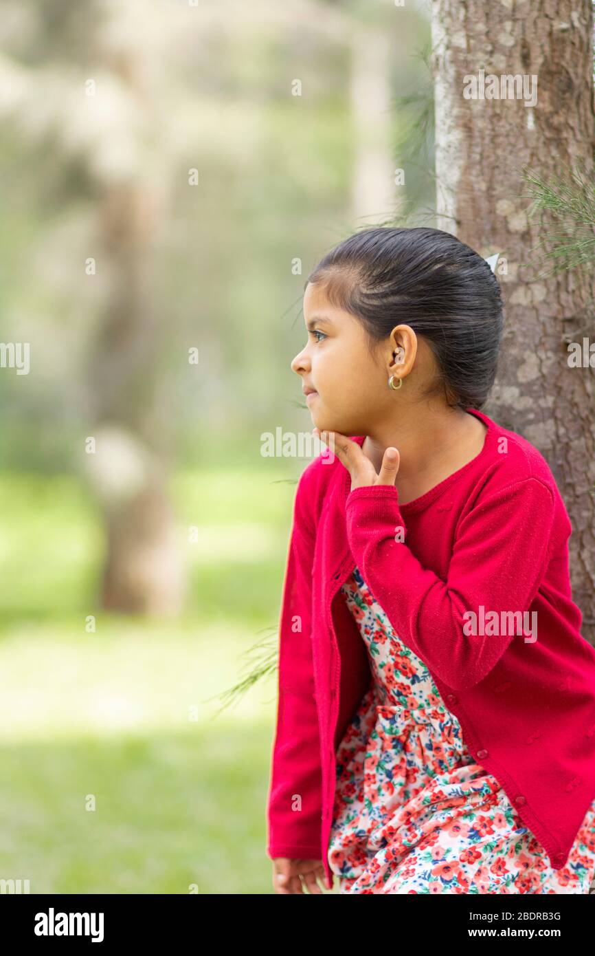 Kleines Mädchen in Blumenkleid und roten Pullover, sehr glücklich und lächelnd im Wald Stockfoto