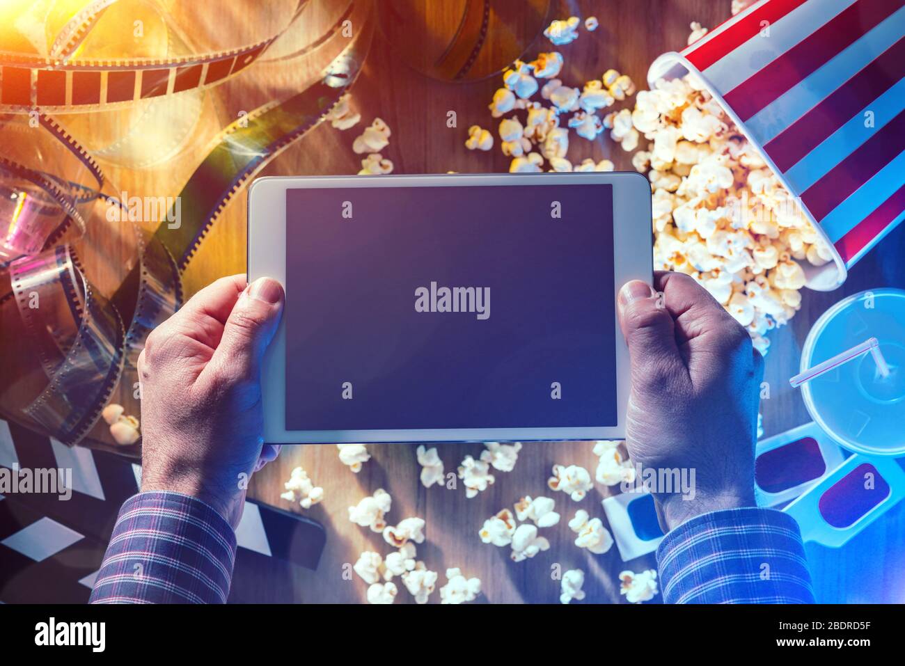 Hände, die ein digitales Touchscreen-Tablet mit Popcorn, 3D-Brille und Filmstreifen halten; Online-Streaming-Kino- und Unterhaltungskonzept für Filme Stockfoto