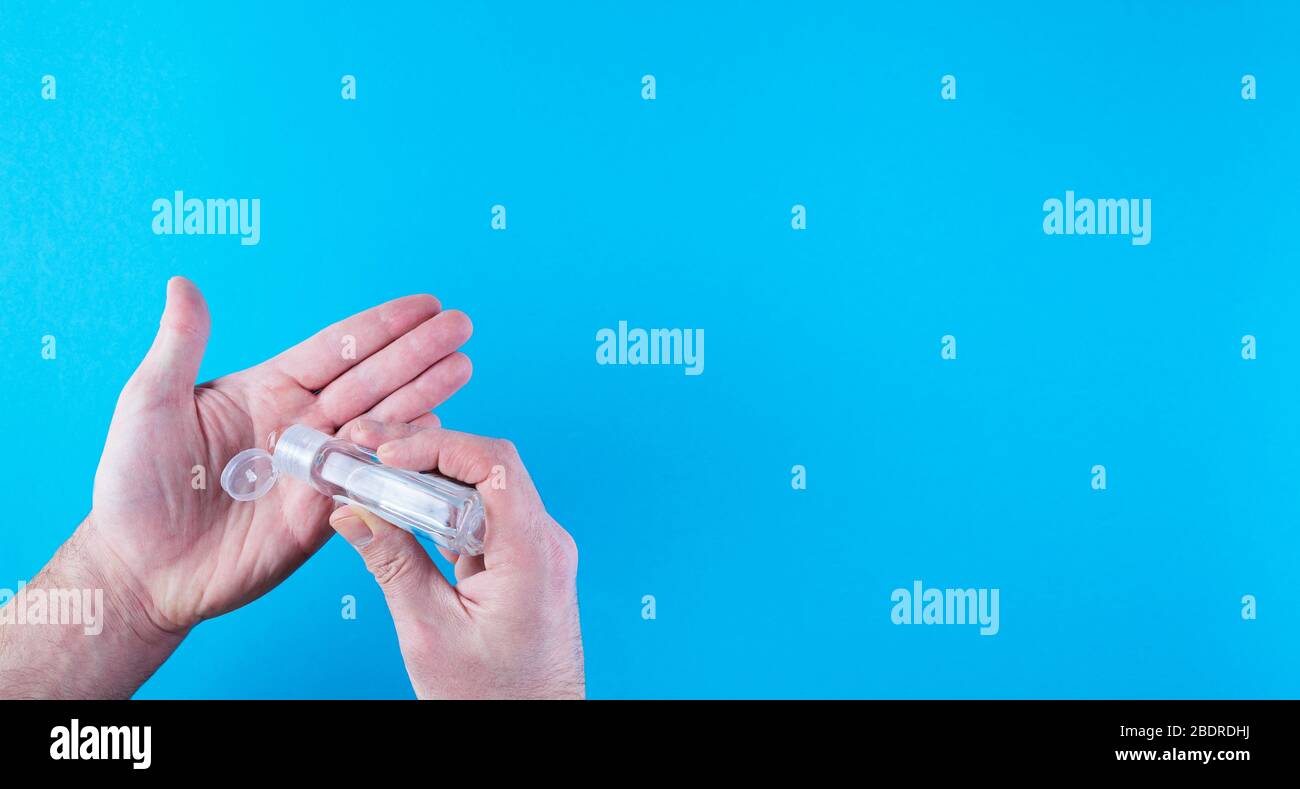 Über Nahaufnahme der Person, die antivirales Händedesinfektionsmittel auf die Hände vor blauem Hintergrund aufgibt Stockfoto