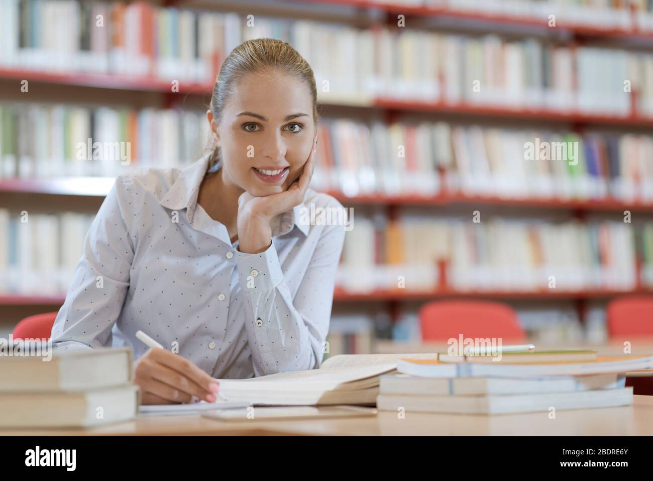 Lächelnd Studentin in der Bibliothek, sitzt sie am Schreibtisch und Studium, Ausbildung und Selbstverbesserung Konzept Stockfoto