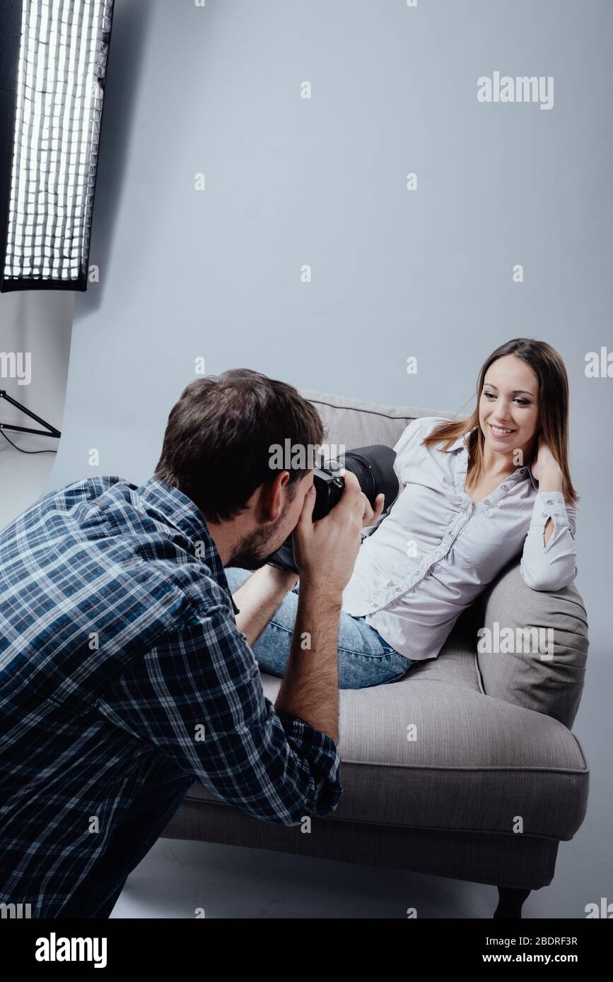 Professionelles Fotoshooting im Studio, ein weibliches Model posiert auf einen Sessel und lächelnd; der Fotograf die Bilder mit seiner digitalen kam Stockfoto