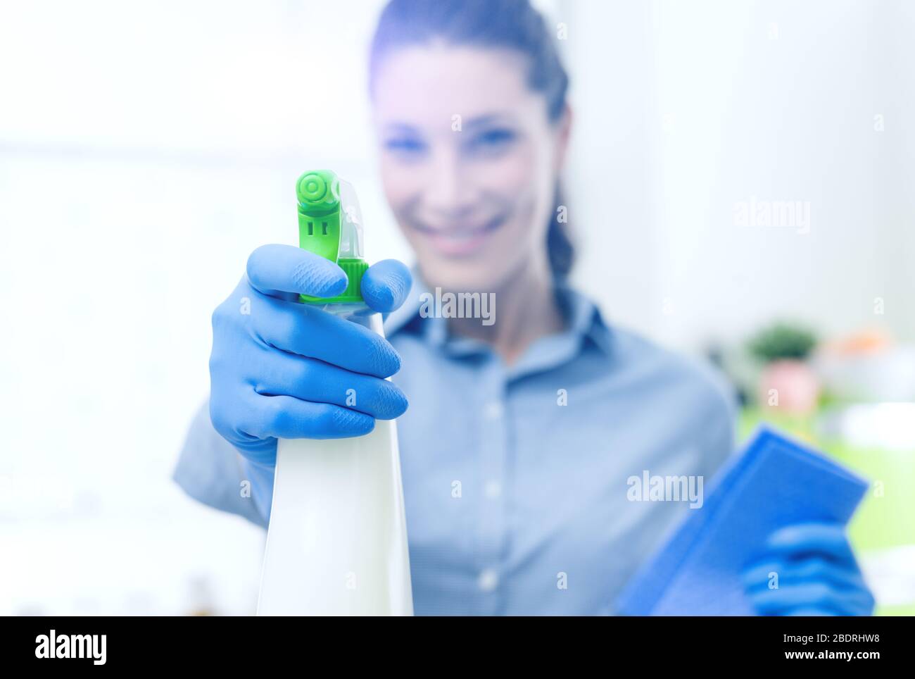 Lächelnde junge Hausfrau macht Arbeit und sprüht ein Reinigungsmittel, Hand und Flasche Nahaufnahme, selektive Fokussierung Stockfoto