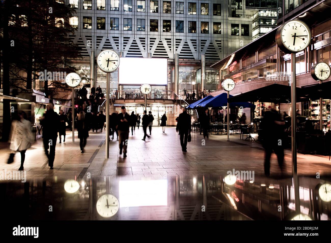 LONDON - Geschäftsleute, die in Canary Wharf an der berühmten Uhr-Installation, Londons Finanzviertel, spazieren gehen Stockfoto