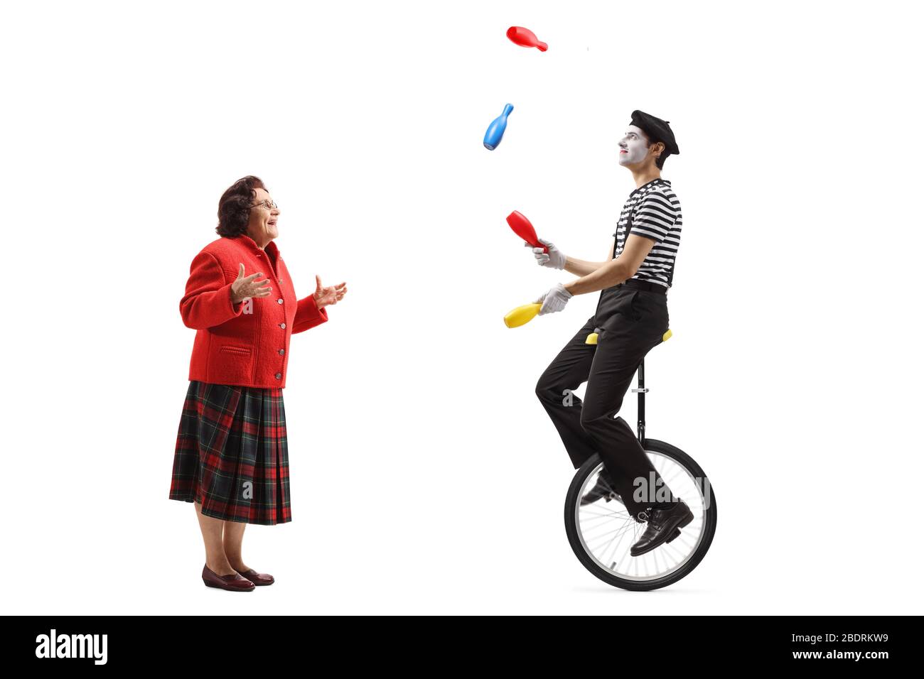 Profilaufnahme in voller Länge von einer älteren Frau, die einen MIME beobachtet, der einen Mono-Zyklus reitet und isoliert auf weißem Hintergrund jongliert Stockfoto