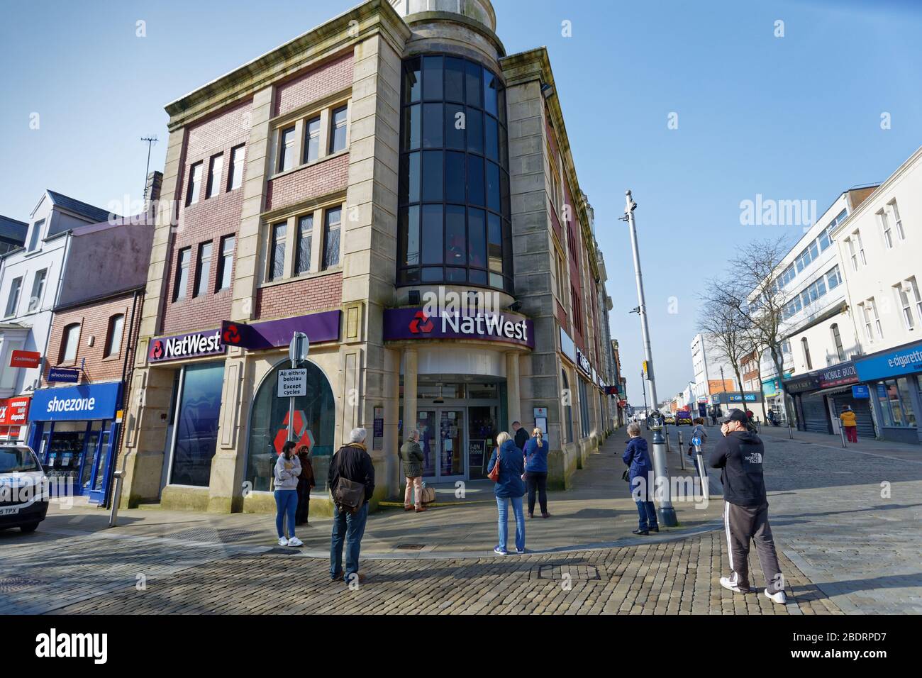 Im Bild: Eine Schlange von Kunden, die die Regeln der sozialen Distanzierung außerhalb der NatWest Bank in Oxford Street, Swansea, Wales, Großbritannien, beobachten. Dienstag, 24. März 2020 Re: Stockfoto
