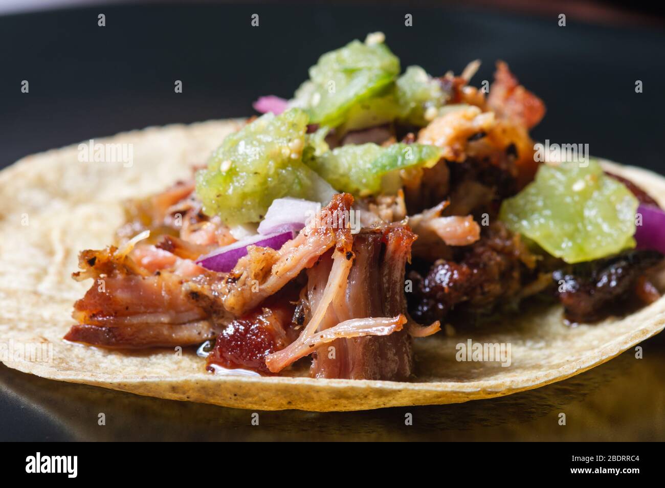 Carnitas Tacos mit roten Zwiebeln und roher Salsa verde. Mexikanische langsam gekochte Schweinefleisch Gericht auf schwarzem Teller isoliert Stockfoto