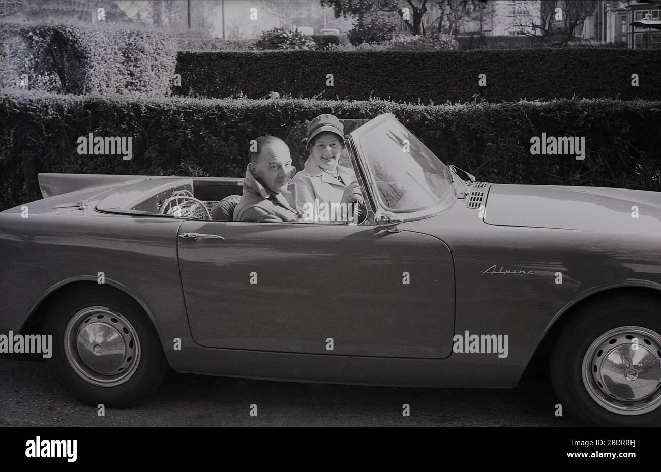 1960er Jahre, historisch, Autofahren in dieser Zeit, ein Paar mittleren Alters sitzt in ihrem Sunbeam Alpine Sportwagen auf einer Auffahrt in Eastholm Green, Letchworth Garden City, Herts, England, Großbritannien geparkt. Die Produktion der Rootes Group umfasste die Jahre 1953-1975, wobei das Fahrzeug aus der Serie I-IV von 1959 bis 1968 zu sehen war. Stockfoto