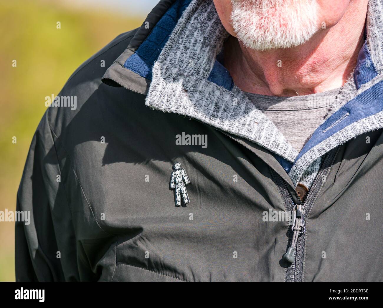 Älterer Mann mit grauem Bart, der den Prostate Cancer UK Charity Badge Pin trägt, der an der Jacke befestigt ist, um das Bewusstsein für die allgemeine Gesundheit zu schärfen, Großbritannien Stockfoto