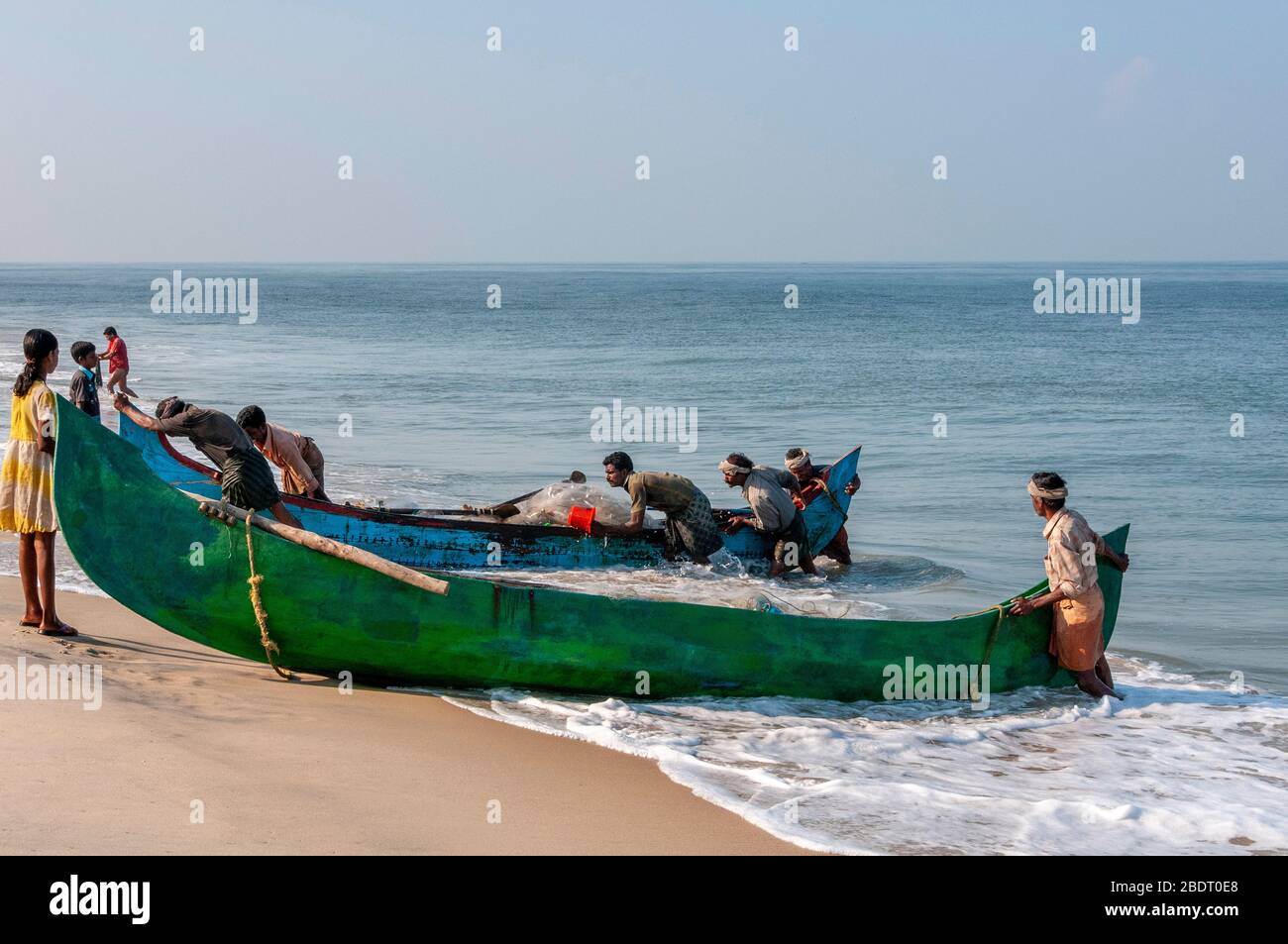 Fischer schleppen ihr traditionelles Holzboot vom Meer am Marari Beach nach einem frühmorgendlichen Angelausflug. Kerala, Indien Stockfoto